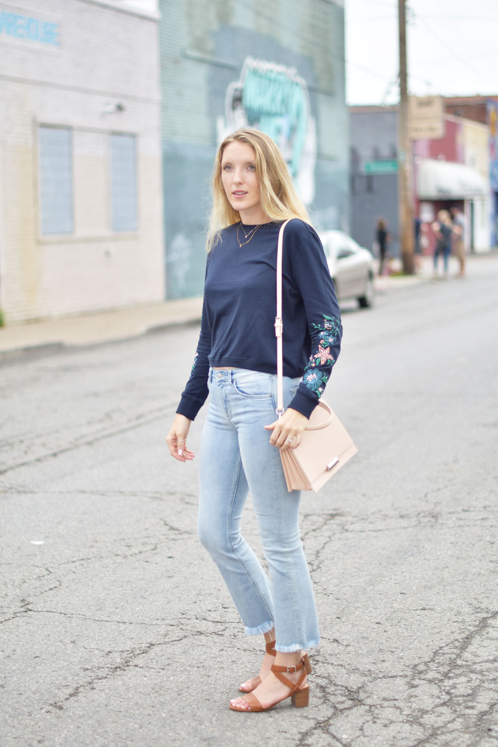 Leslie Musser wears kick flare denim with an embroidered sweatshirt and structured blush purse on one brass fox