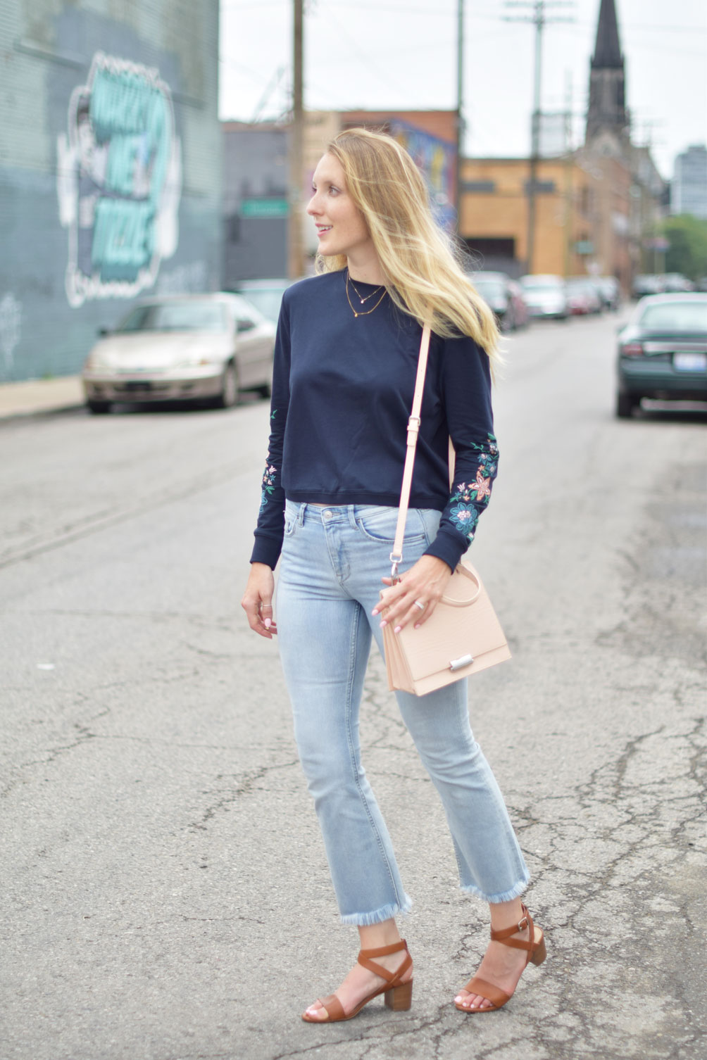 Leslie Musser wears kick flare denim with an embroidered sweatshirt and structured blush purse on one brass fox