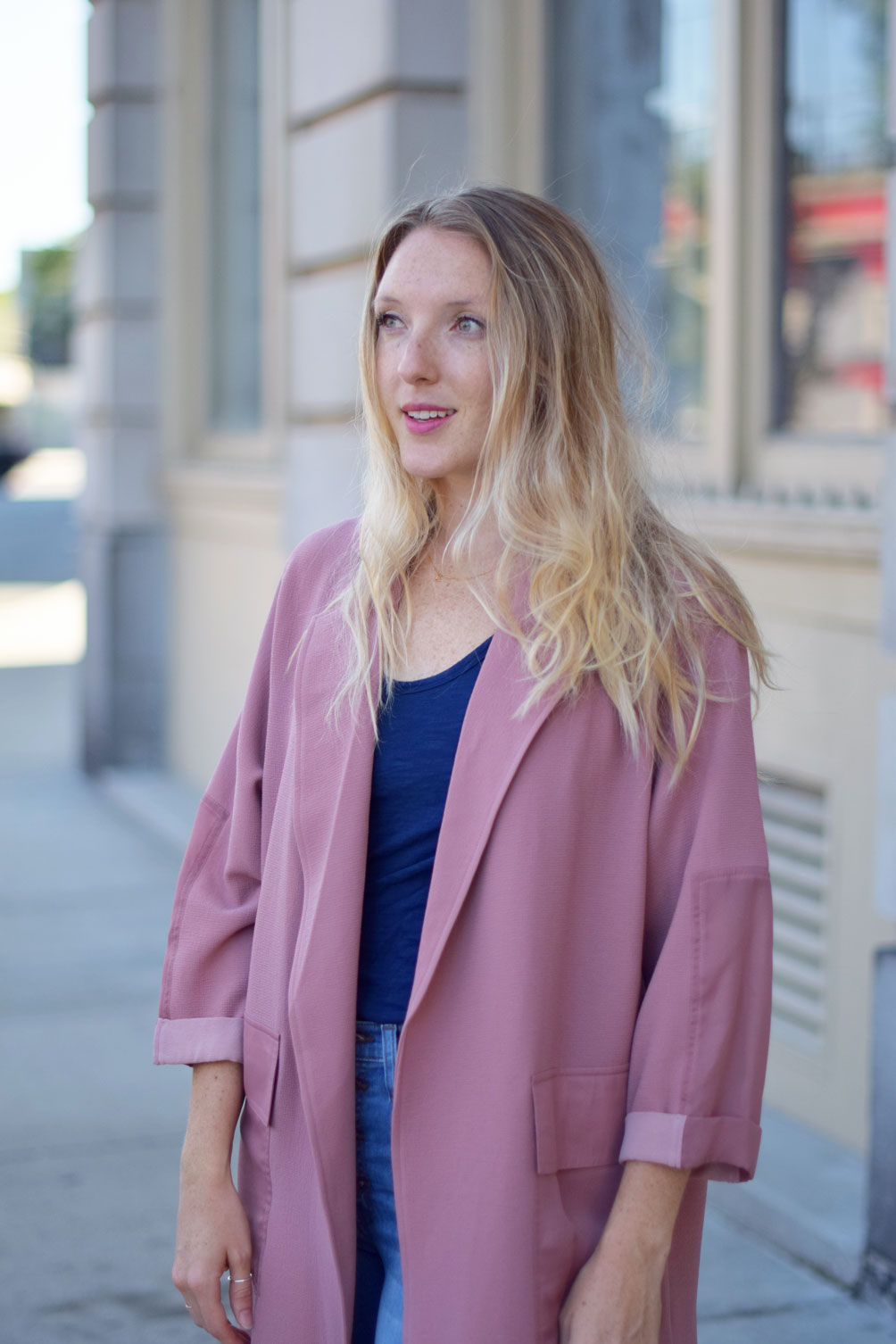 Leslie Musser wears a paneled duster coat with button-fly jeans and pink sneakers on one brass fox