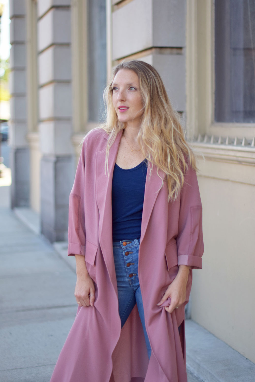Leslie Musser wears a paneled duster coat with button-fly jeans and pink sneakers on one brass fox