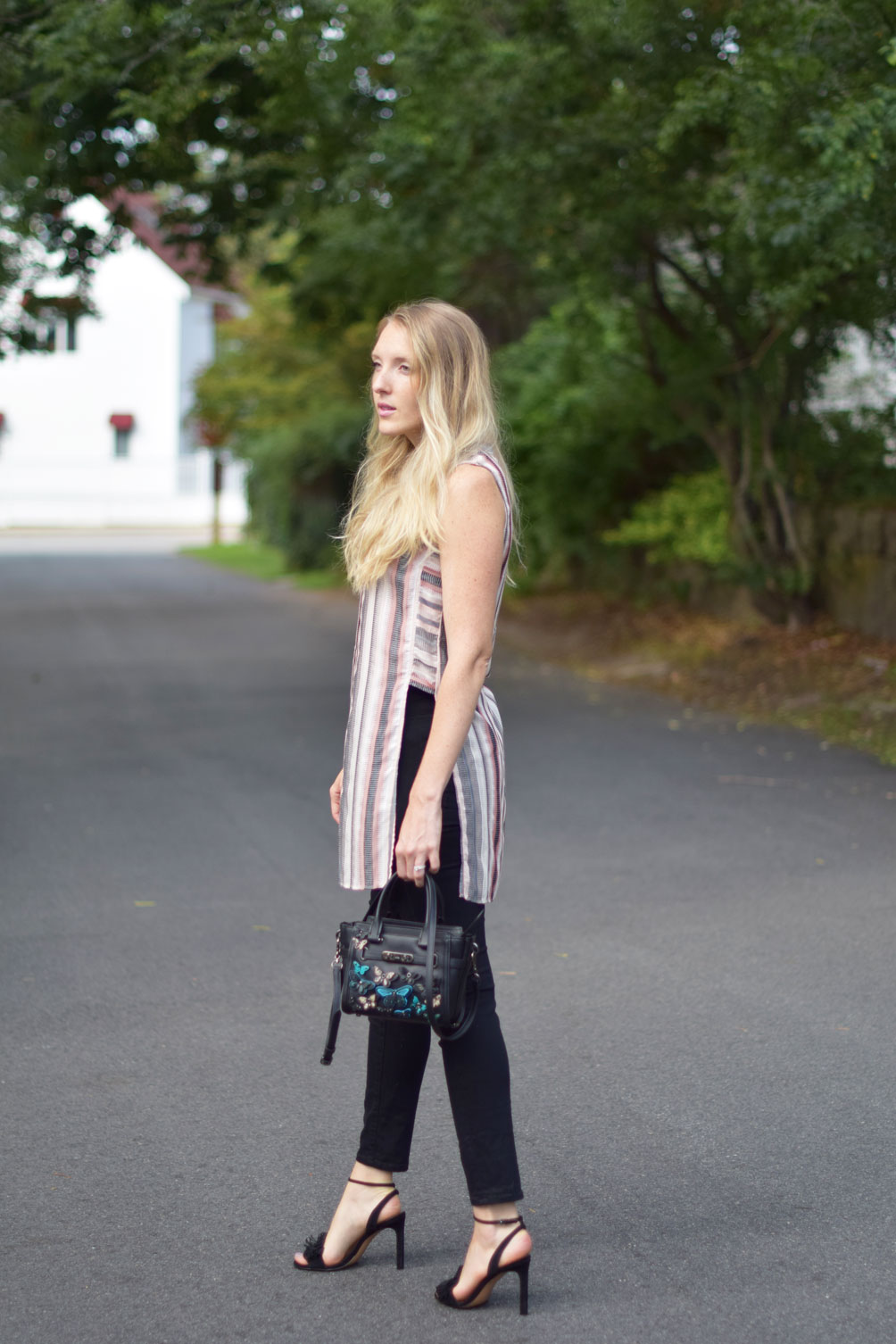 Leslie Musser wears a sleeveless tunic top with black skinny jeans and a butterfly embellished Coach bag on one brass fox