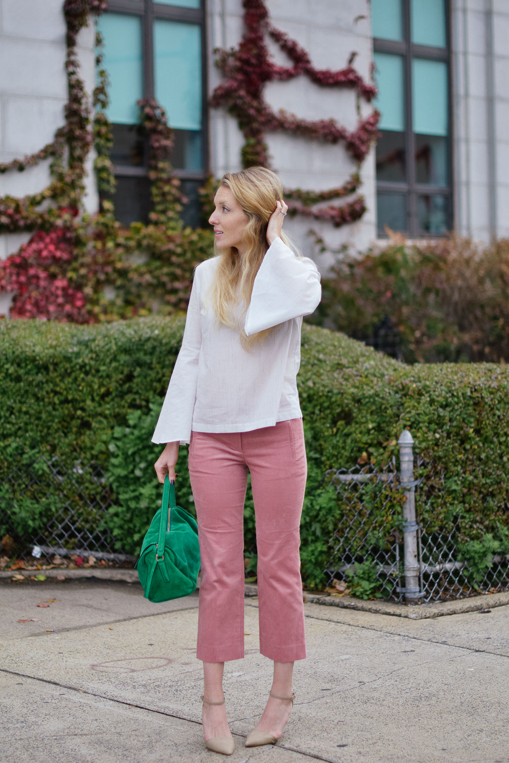 Leslie Musser wears cropped blush corduroys with a striped bell sleeve top and emerald tote on one brass fox