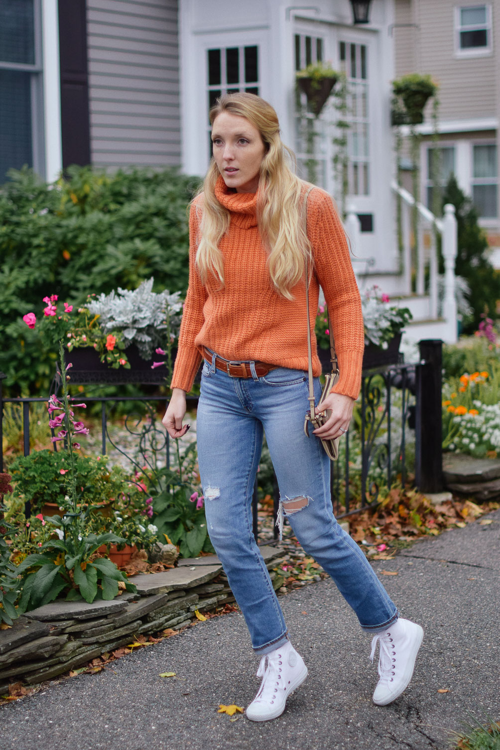 Leslie Musser dressing for sweater weather in an orange turtleneck and real straight jeans with high top sneakers on one brass fox