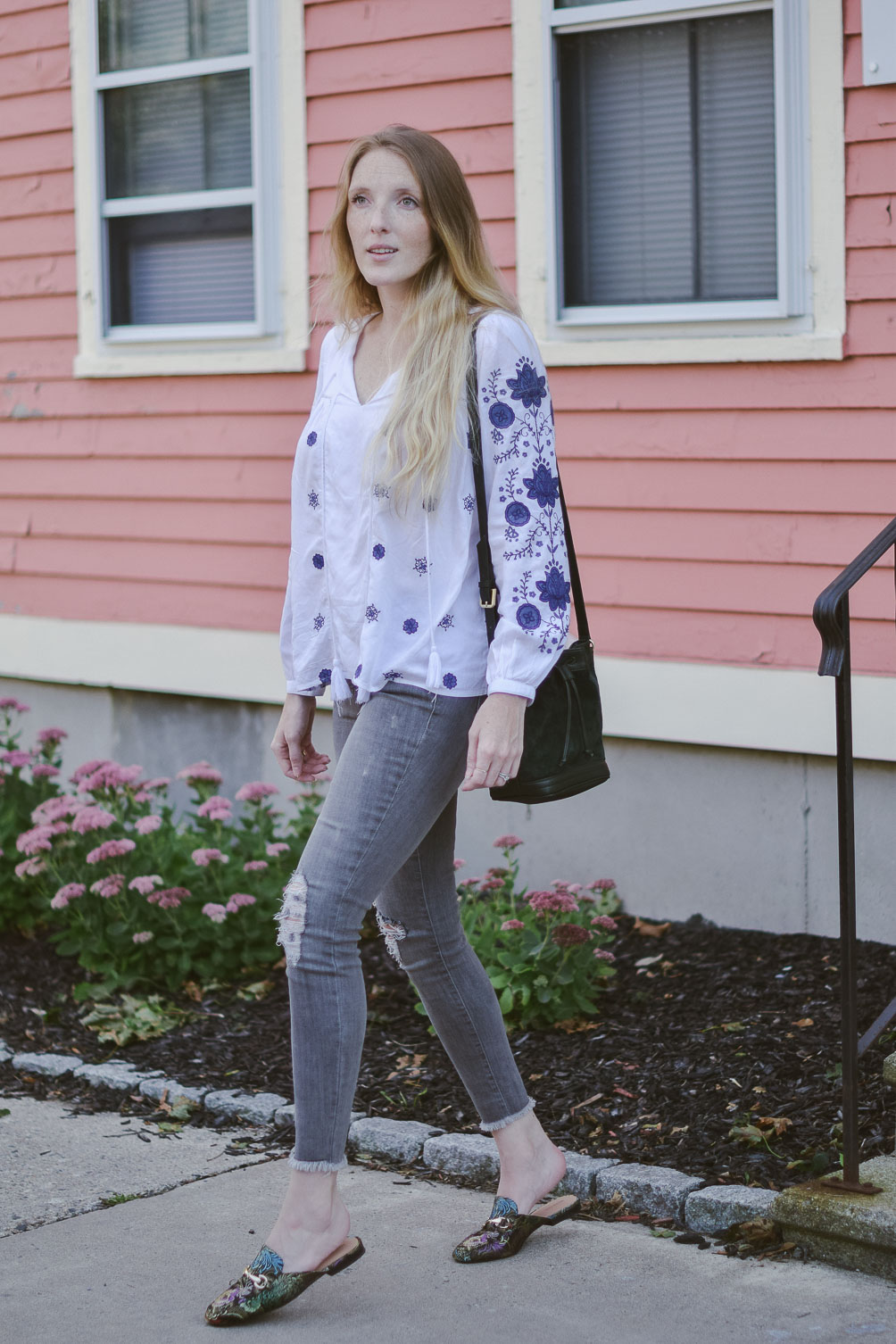 fashion blogger Leslie Musser styling the best bohemian tops for fall with gray denim, printed slides, and a suede bucket bag