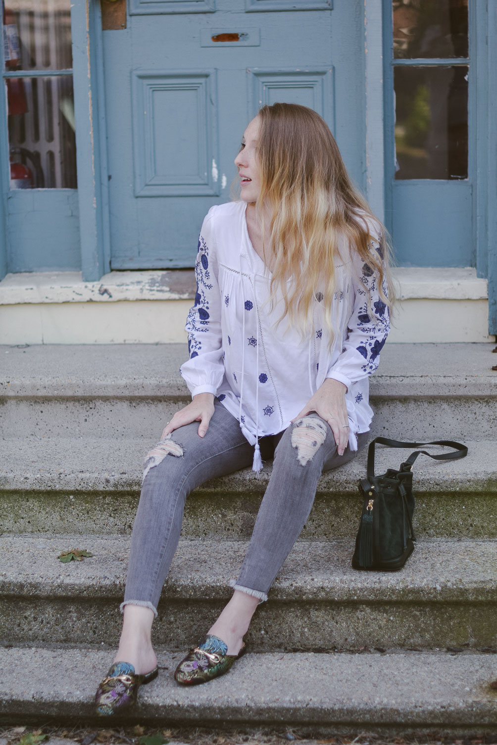 fashion blogger Leslie Musser styling the best bohemian tops for fall with gray denim, printed slides, and a suede bucket bag
