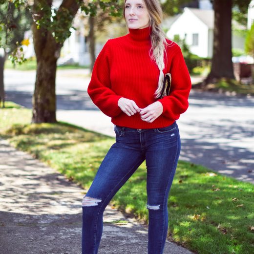 wearing a bright chunky red sweater with step hem jeans and block heel sandals