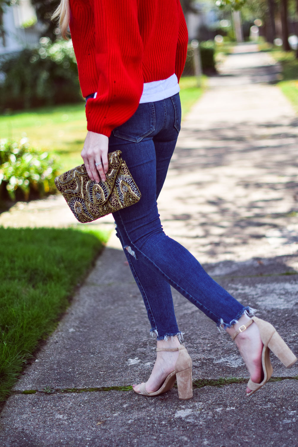 wearing a bright chunky red sweater with step hem jeans and block heel sandals