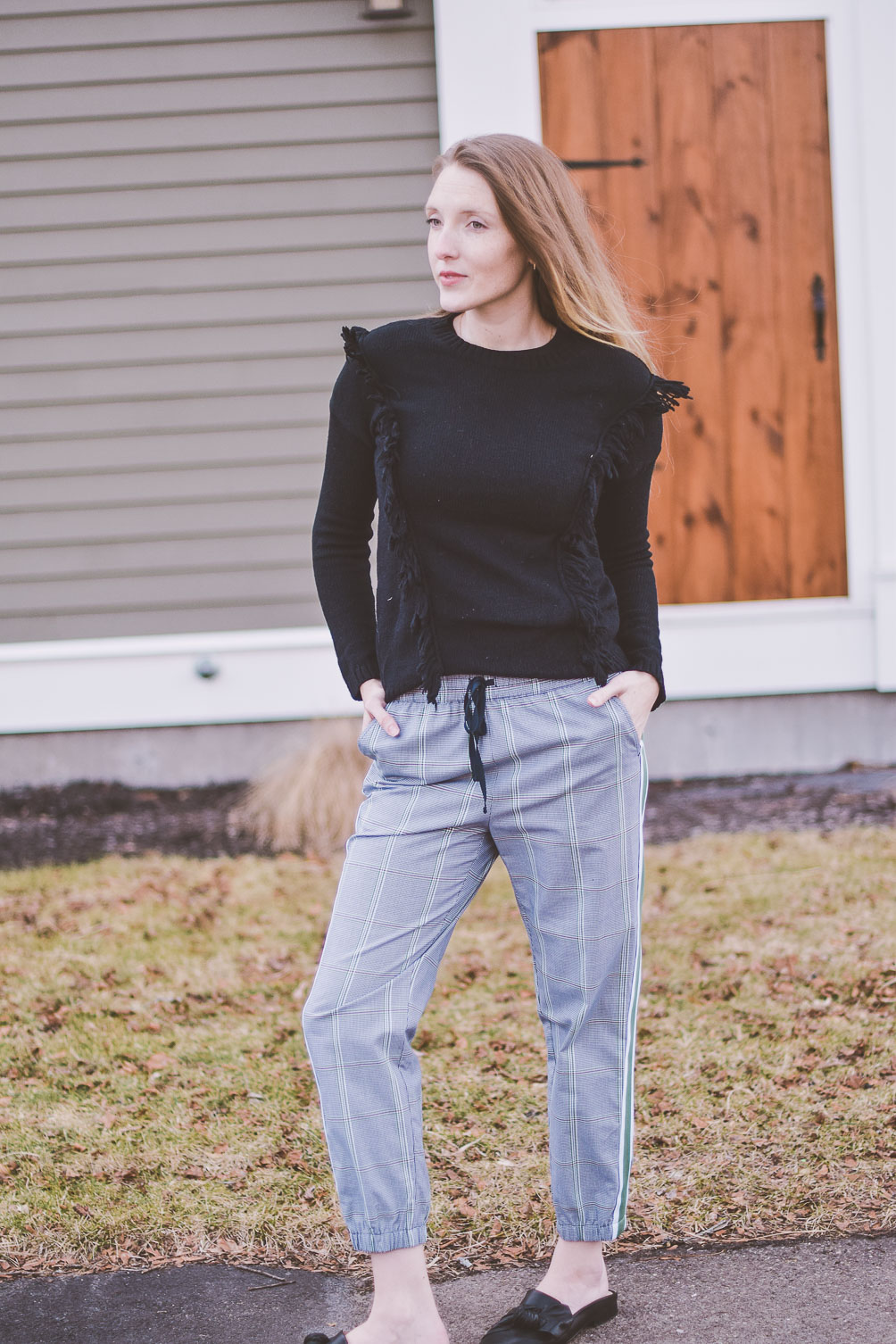 styling a modern checked track pants for everyday wear with black leather mules and a fringe sweater